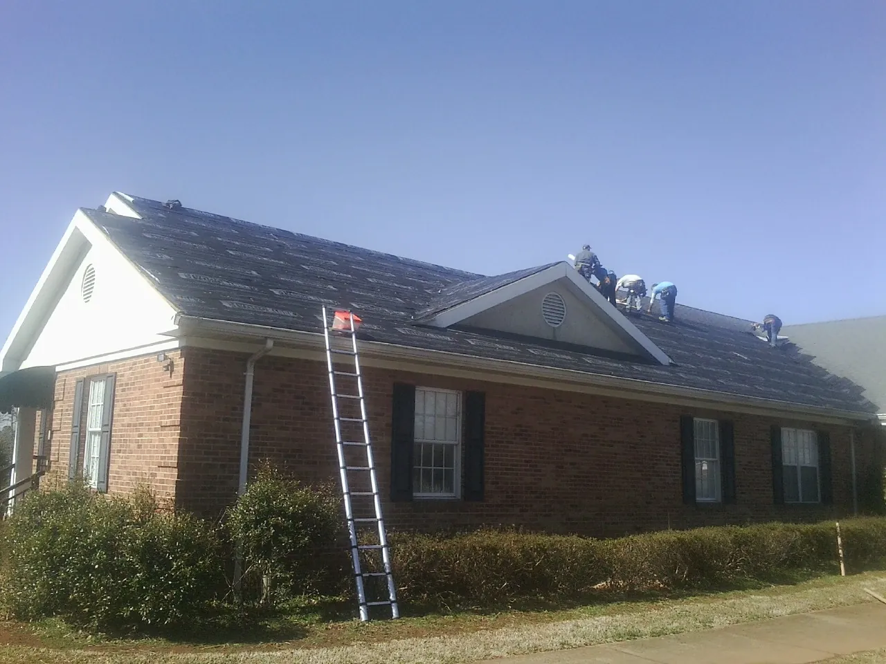 Crew tearing shingles off a brick ranch roof with a ladder set — Emergency Roof Repair work by our crew in Marshfield