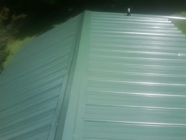 New green metal panels meeting at the ridge of a roof — Flat Roof Repair work by our crew in Marshfield